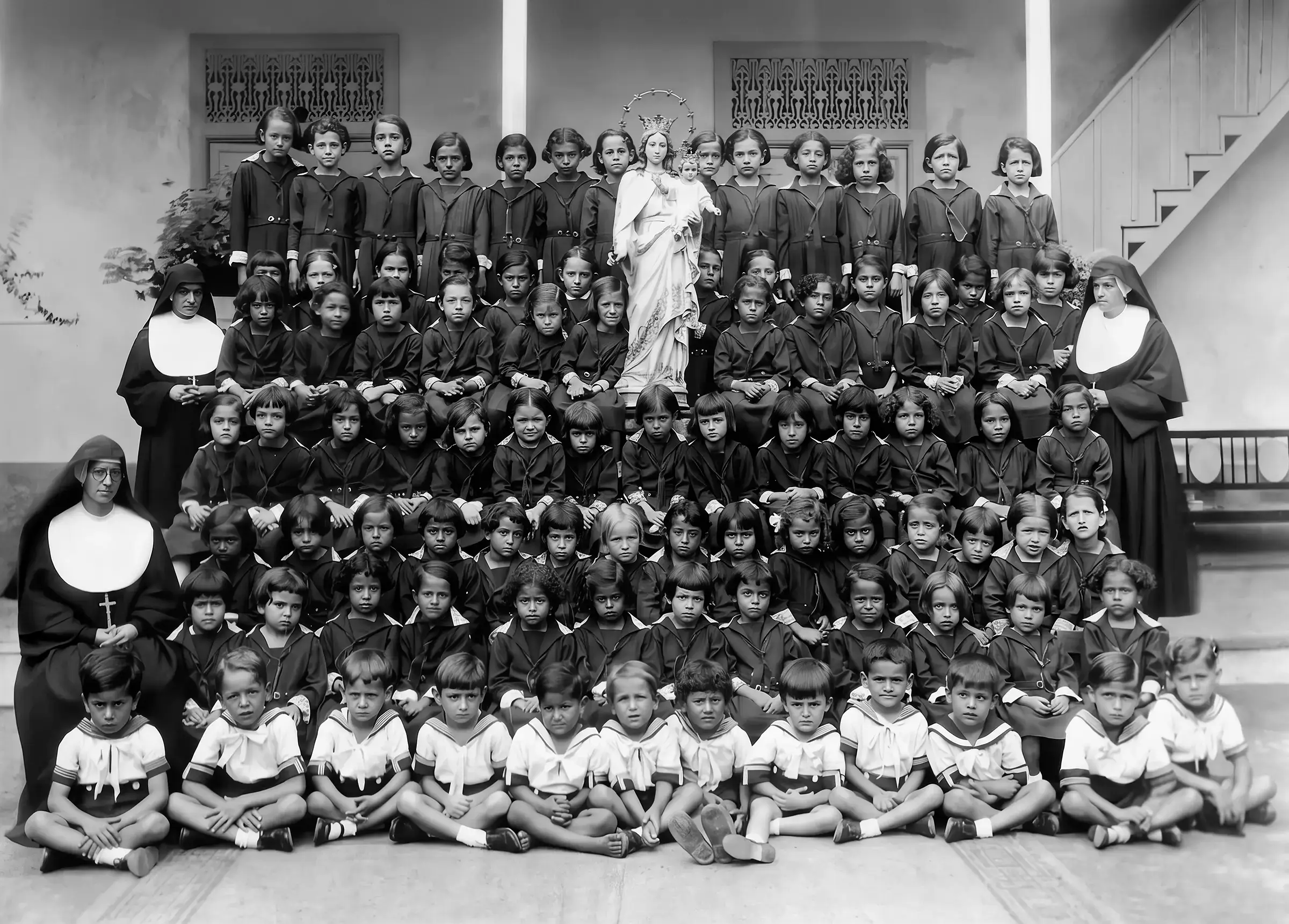 Retrato escolar de un numeroso grupo de niños y niñas con varias religiosas, dispuestos en filas alrededor de una imagen de la Virgen.