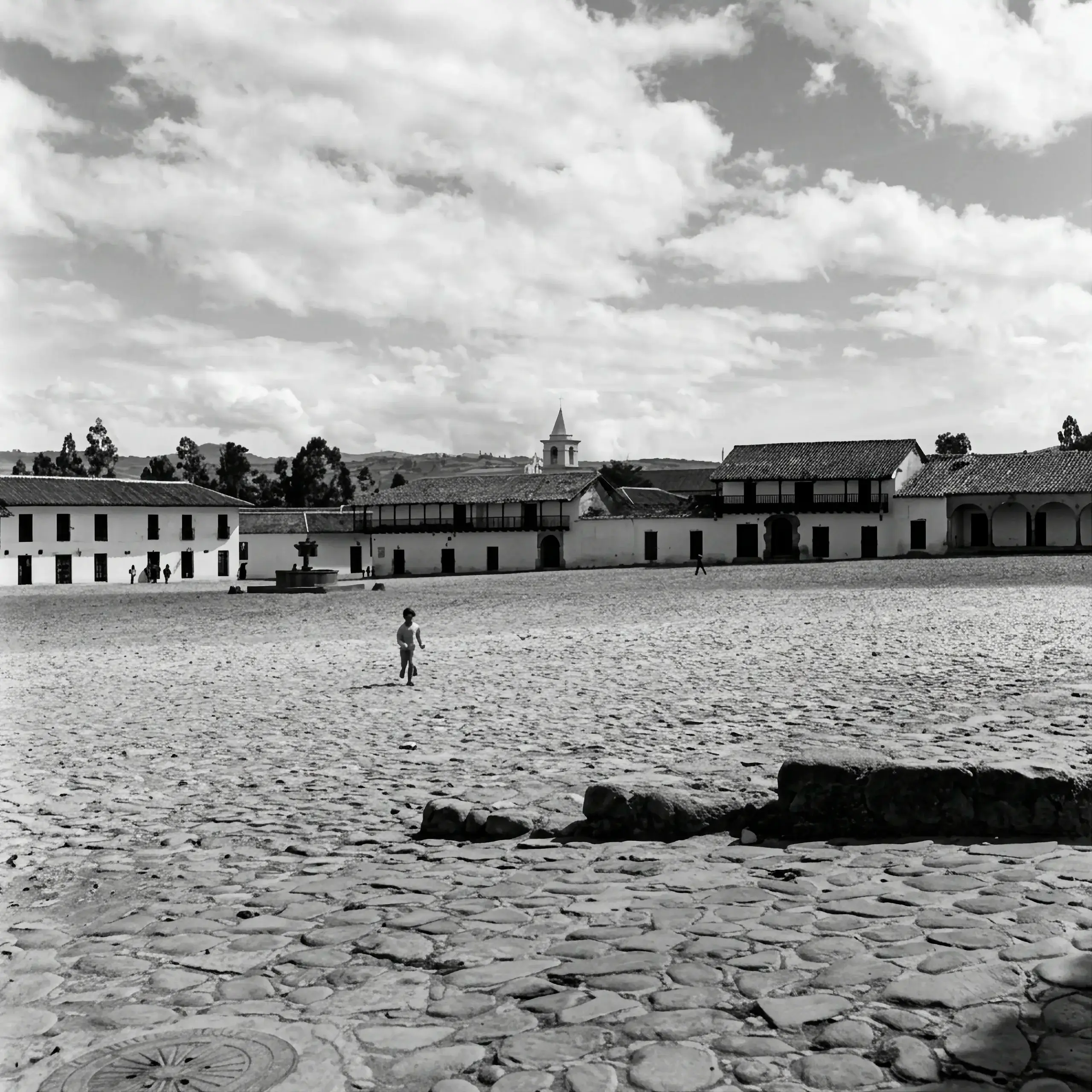 Amplia plaza empedrada de Villa de Leyva, rodeada de casas blancas de teja, con un niño cruzándola.