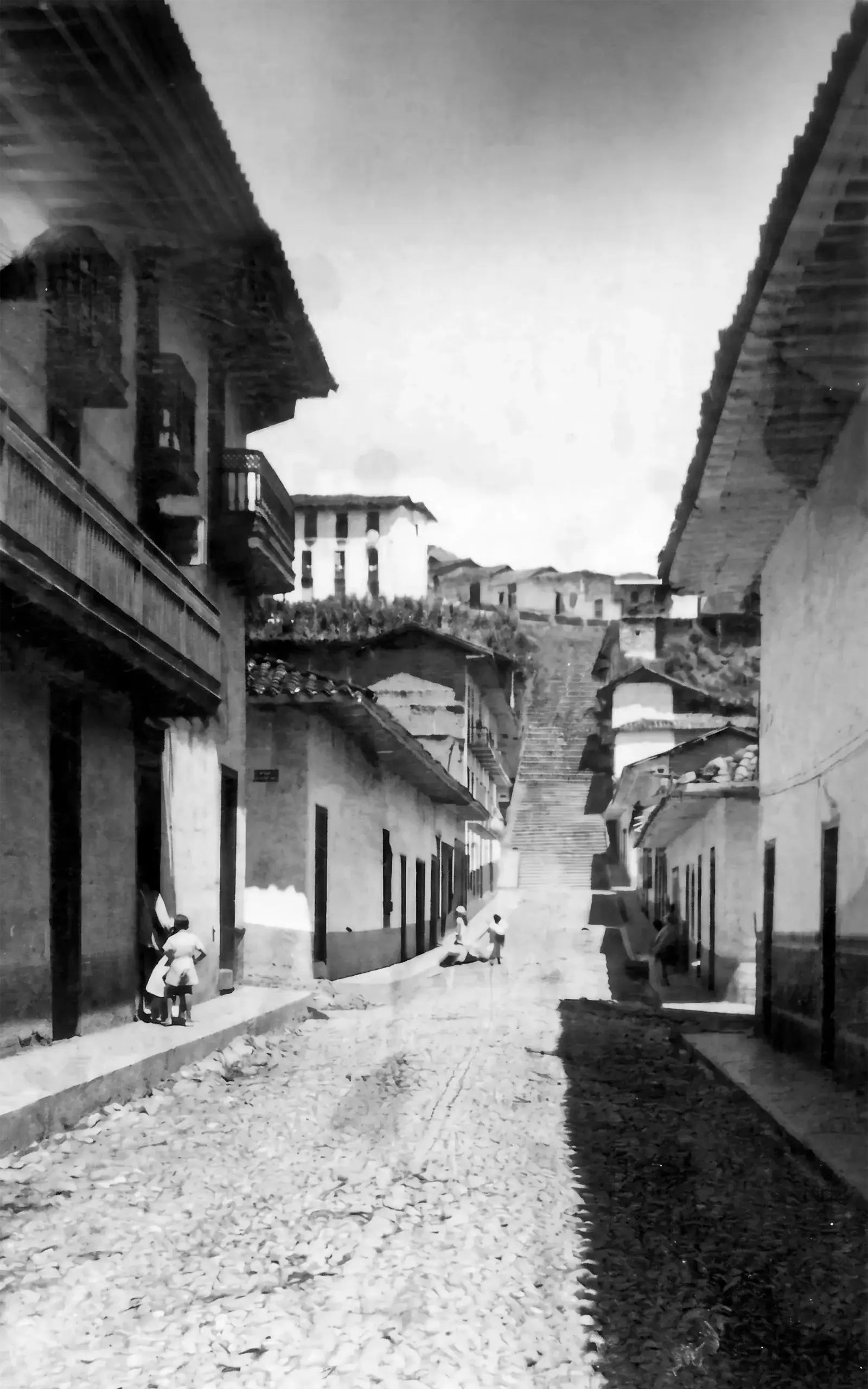 Calle de Andes empedrada en pendiente, entre casas con balcones de madera y aleros de teja.