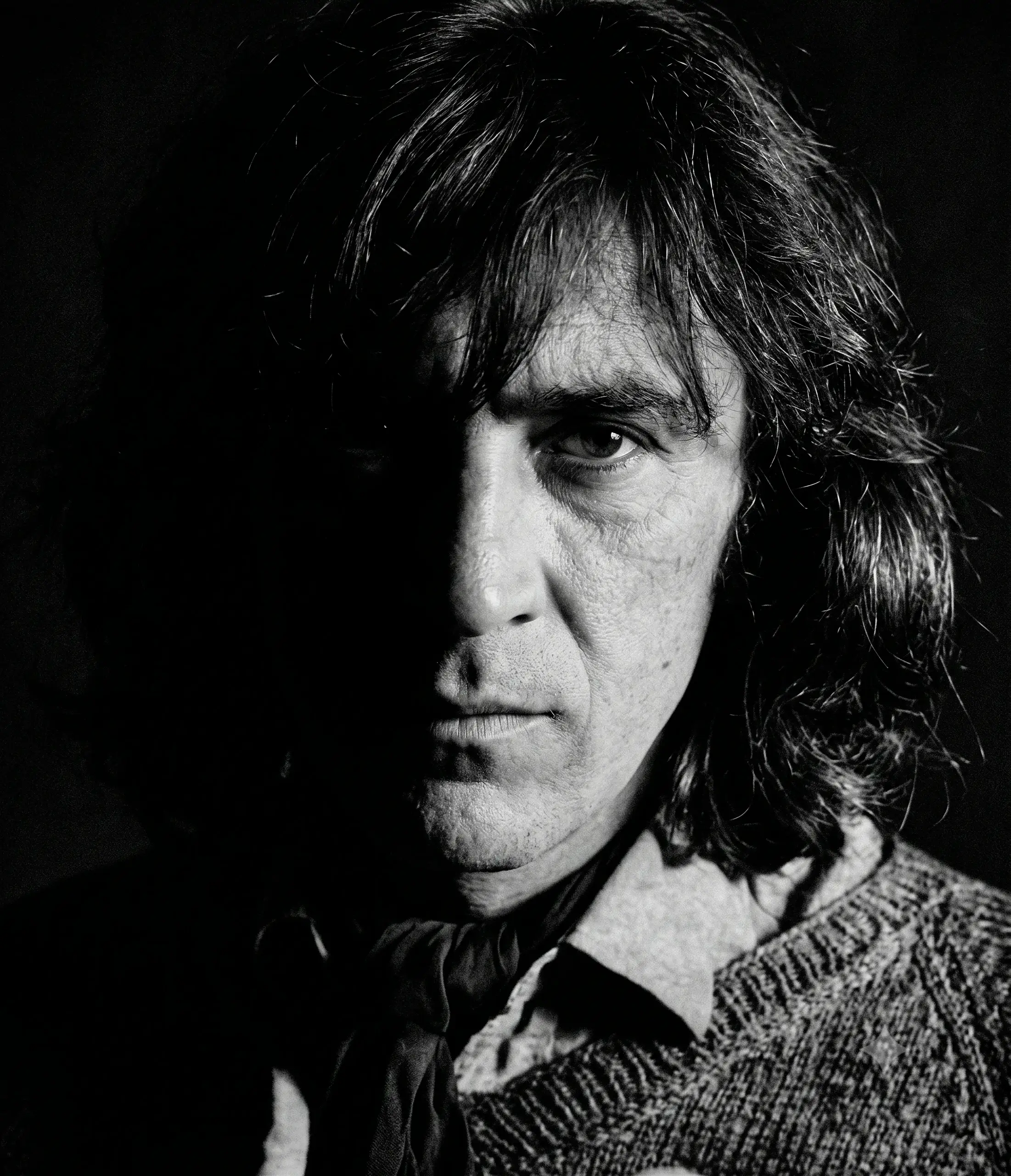 Retrato de Gonzalo Arango con cabello largo, una mitad del rostro iluminada y la otra en sombra.