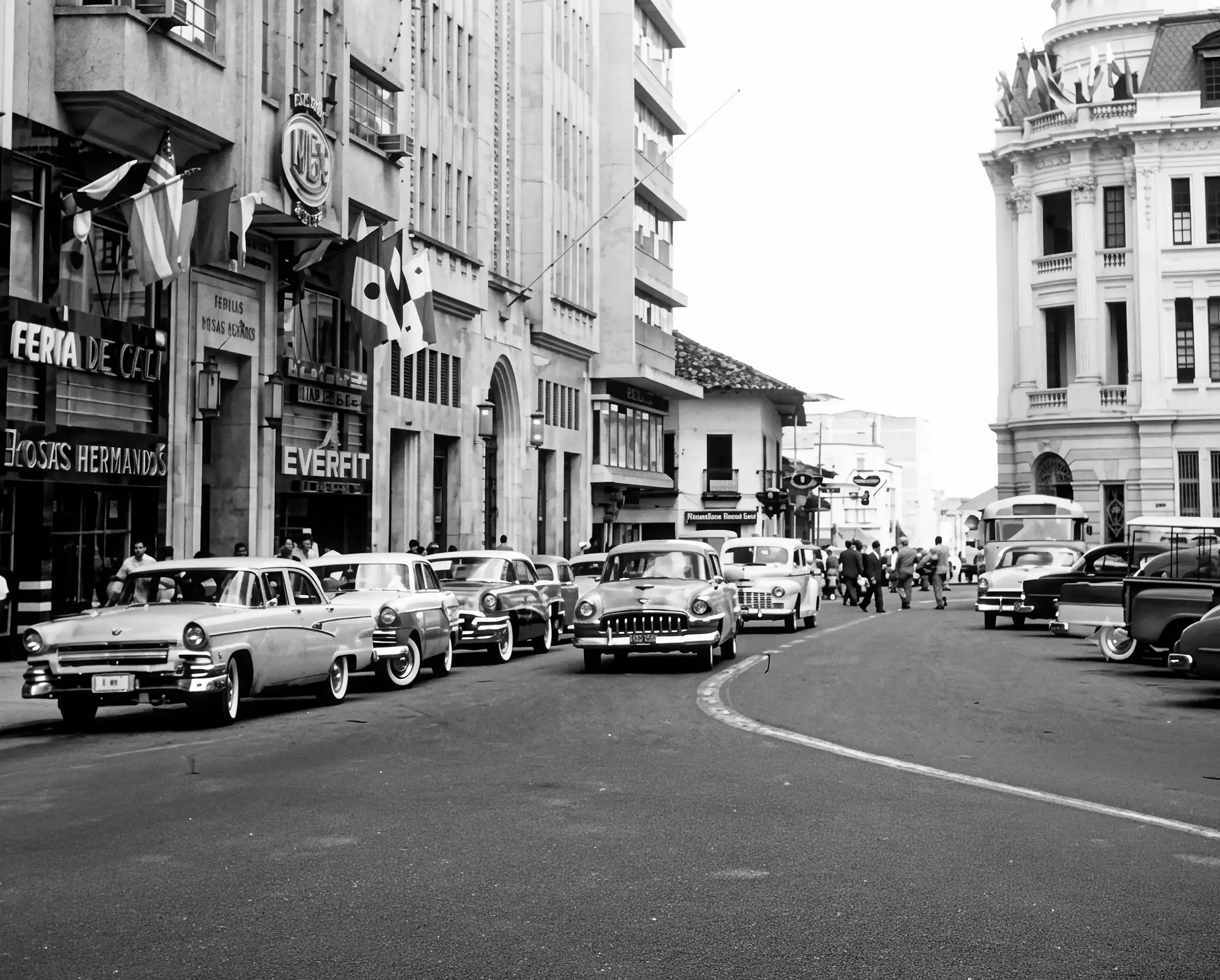 Calle comercial de Cali con automóviles de época, letreros y peatones, flanqueada por edificios de distintas alturas.